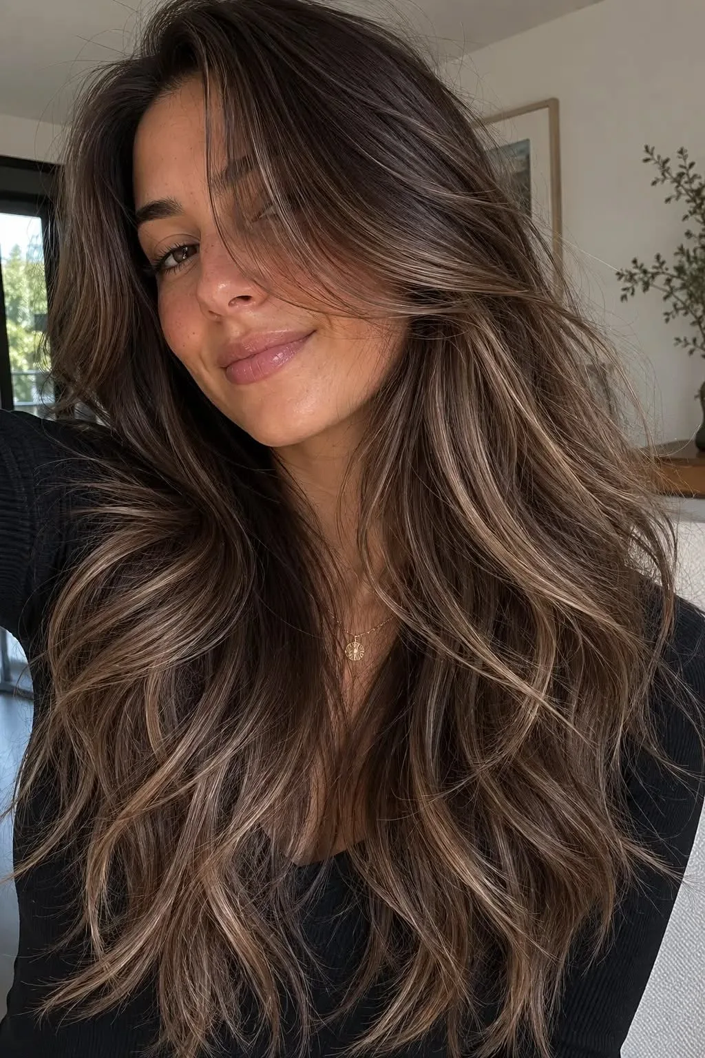 Eine junge Frau mit langem, braunem Haar, das durch sanfte, hellere Balayage-Highlights natürlich aufgehellt ist.