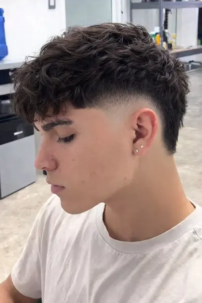 Ein junger Mann im Profil mit einem Textured Fade Haarschnitt, der welliges Oberhaar mit einem präzisen Übergang zeigt.
