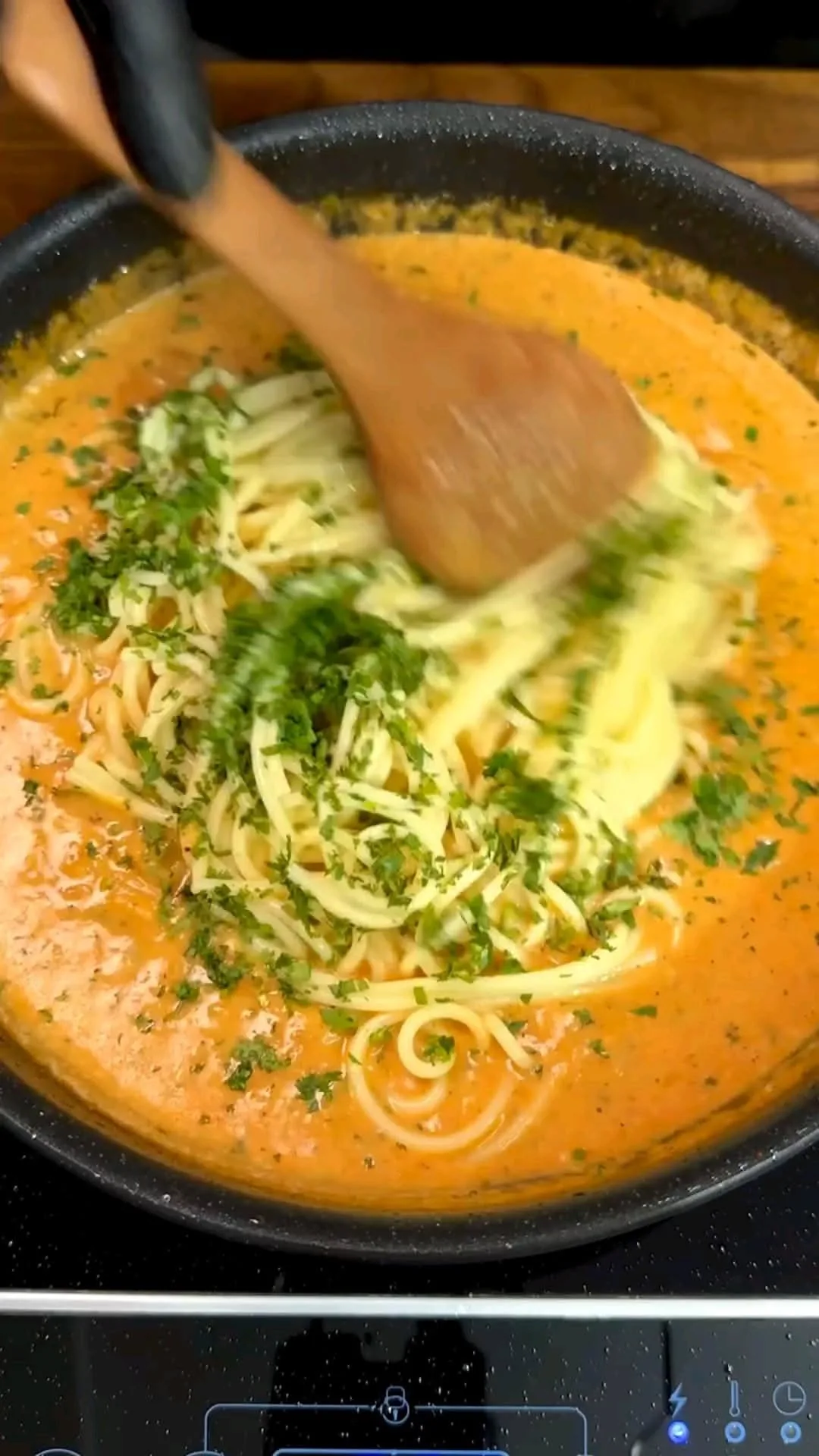 Spaghetti werden in einer schwarzen Pfanne mit einer cremigen Tomaten-Sahne-Sauce und Kräutern vermengt.