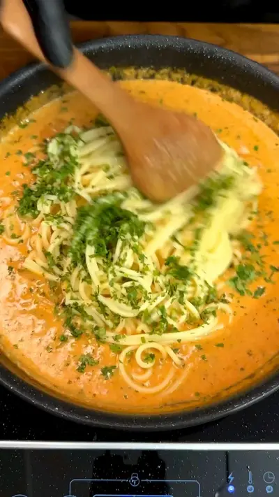 Spaghetti werden in einer schwarzen Pfanne mit einer cremigen Tomaten-Sahne-Sauce und Kräutern vermengt.