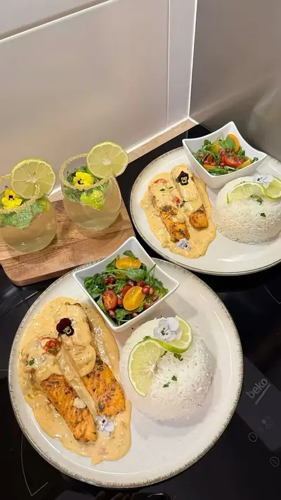Deux assiettes de saumon sauce crémeuse avec du riz et une salade fraîche accompagnées de cocktails décorés.