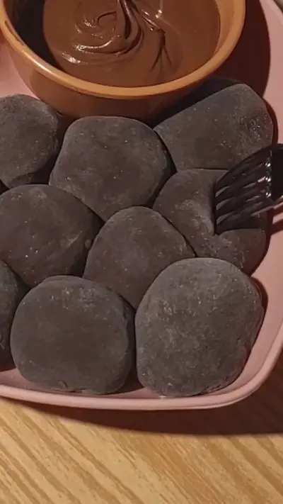 Une assiette rose avec des mochis au cacao et un bol de sauce au chocolat fondant.