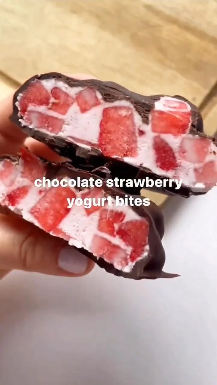 Main tenant deux moitiés d'une bouchée glacée aux fraises et yaourt enrobée d'une fine couche de chocolat noir.
