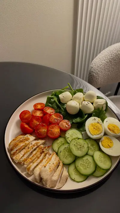 Une assiette composée de poulet grillé, œufs durs, tomates cerises, billes de mozzarella, concombre et épinards.