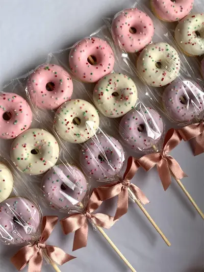 A diagonal arrangement of mini donuts on wooden sticks glazed in pastel colors and tied with rose gold ribbons.