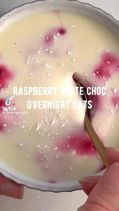 Eine Nahaufnahme cremiger Overnight Oats mit Himbeersoße und weißer Schokolade in einer Schüssel.