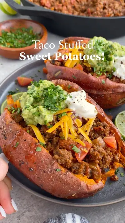 Twee gebakken zoete aardappels op een donker bord, gevuld met gehakt, cheddar, guacamole en verse koriander.