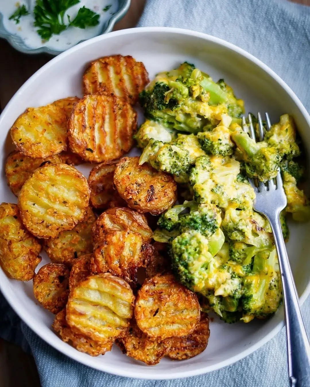 Eine weiße Schüssel mit knusprigen Bratkartoffelscheiben und cremigem Brokkoli-Käse-Gratin, serviert mit einer Gabel.