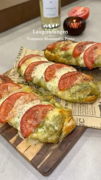 Drei mit Tomaten, Mozzarella und Pesto belegte Laugenstangen liegen auf einem Holzbrett mit Backpapier.