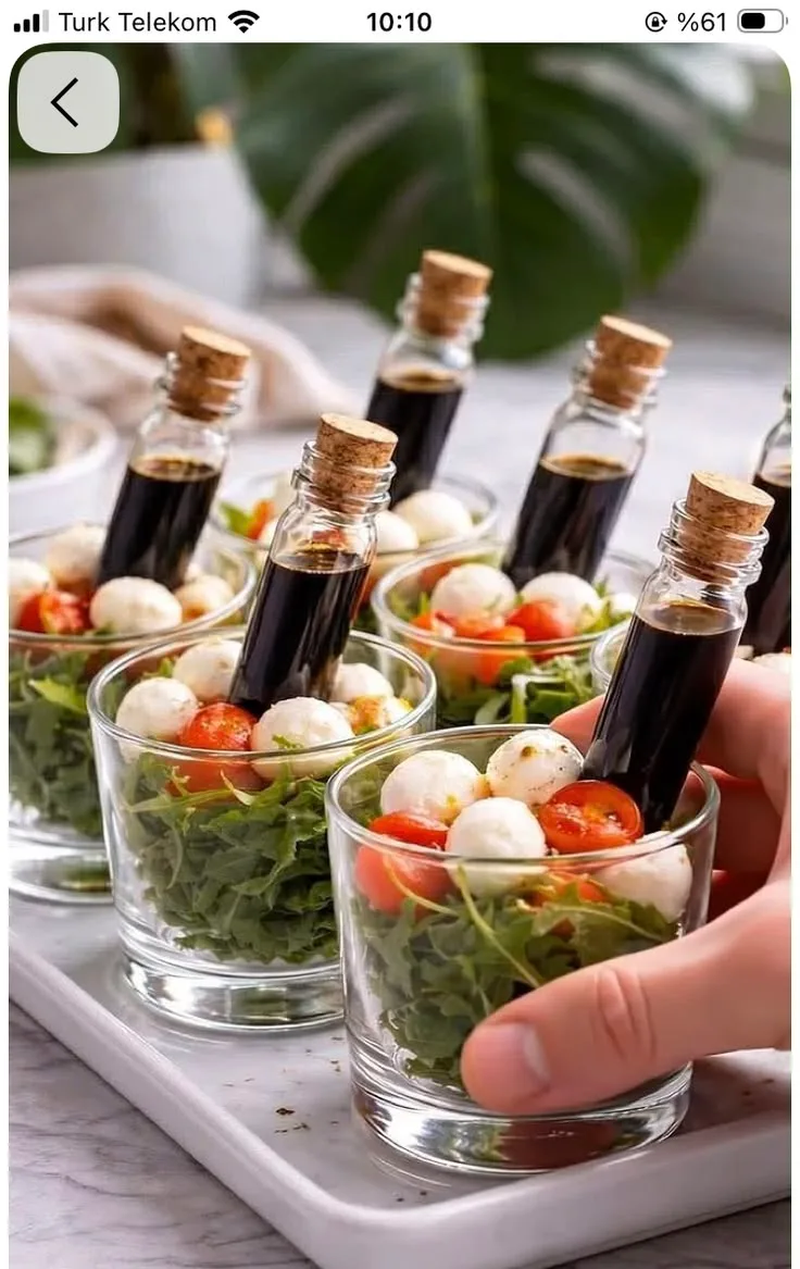 Mehrere kleine Gläser auf einem Tablett gefüllt mit Rucola, Kirschtomaten, Mozzarella und einem Balsamico-Fläschchen.