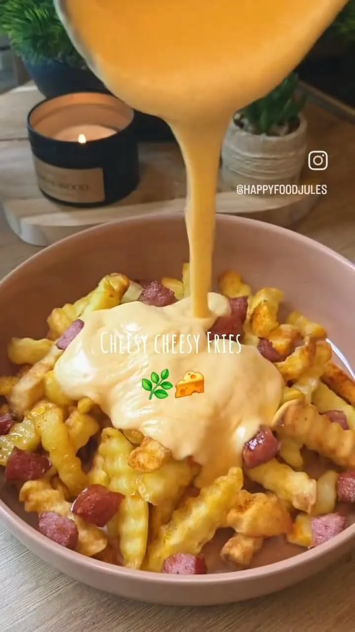 De la sauce au fromage orange est versée sur un bol de frites ondulées parsemées de morceaux de saucisse grillée.