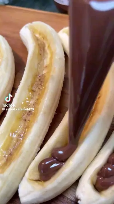 Een close-up van gepelde bananen op een houten plank die met chocoladepasta worden gevuld vanuit een spuitzak.