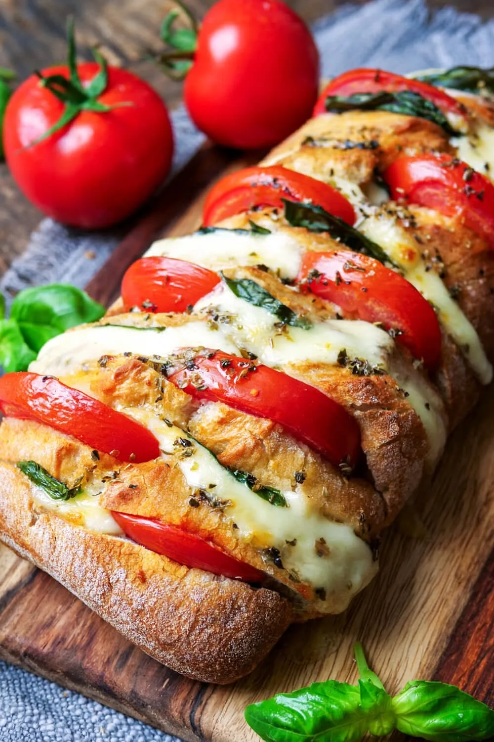 Ein goldbraunes Baguette, gefüllt mit Tomaten, Mozzarella und Basilikum, präsentiert auf einem rustikalen Holzbrett.