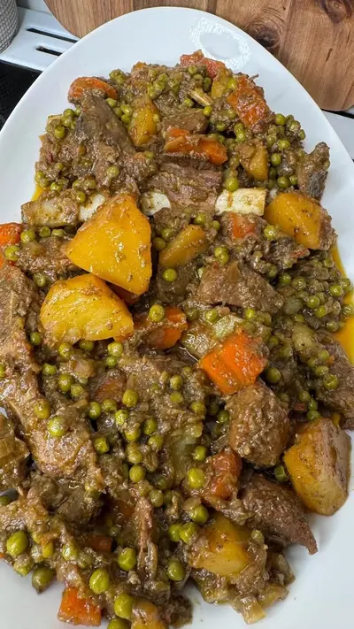 Un grand plat ovale blanc garni d'un ragoût de viande riche avec des petits pois, des carottes et des pommes de terre.