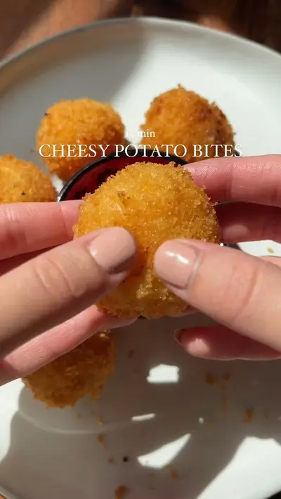 Des mains tiennent une bouchée de pomme de terre dorée et croustillante au-dessus d'une assiette.