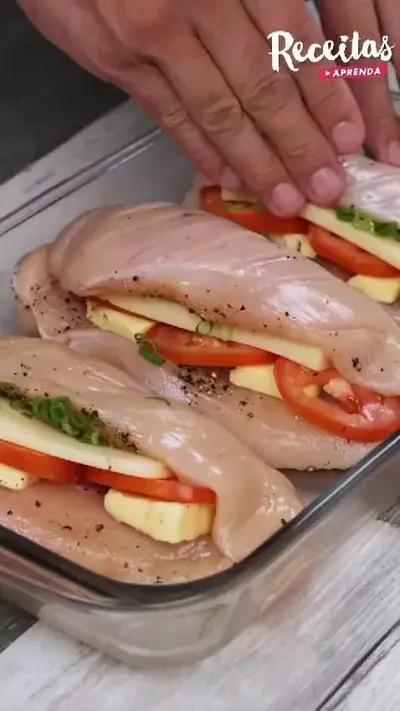 Zwei rohe Hähnchenbrustfilets liegen in einer Glasauflaufform, gefüllt mit Tomatenscheiben und Käsewürfeln.