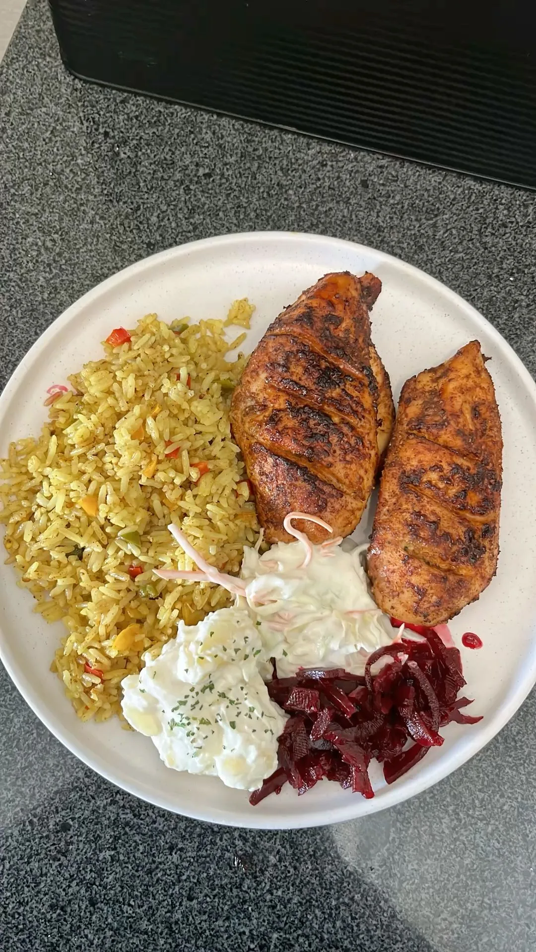 Une assiette composée de poulet grillé, riz aux légumes, salade de pommes de terre, salade de chou et betteraves.