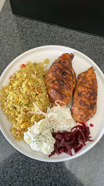 Une assiette composée de poulet grillé, riz aux légumes, salade de pommes de terre, salade de chou et betteraves.