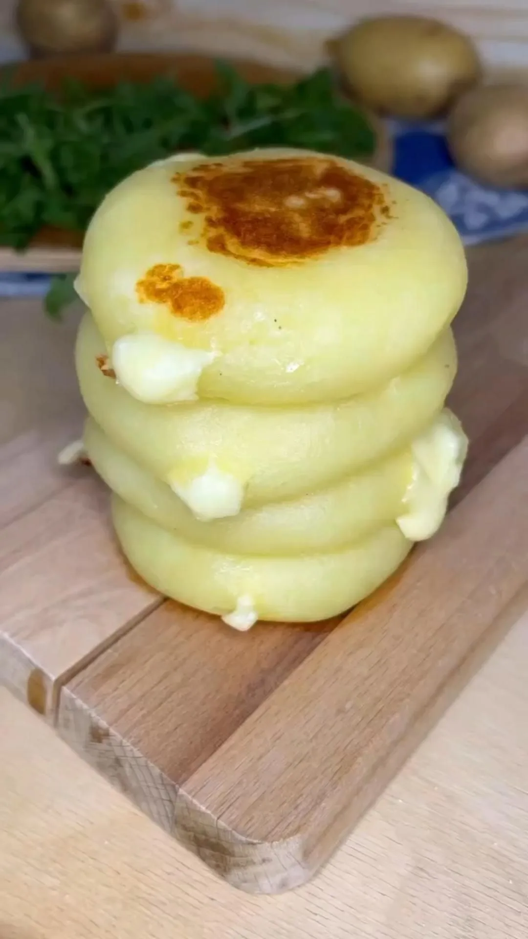 Une pile de quatre galettes de pommes de terre dorées contenant du fromage fondant sur une planche en bois.