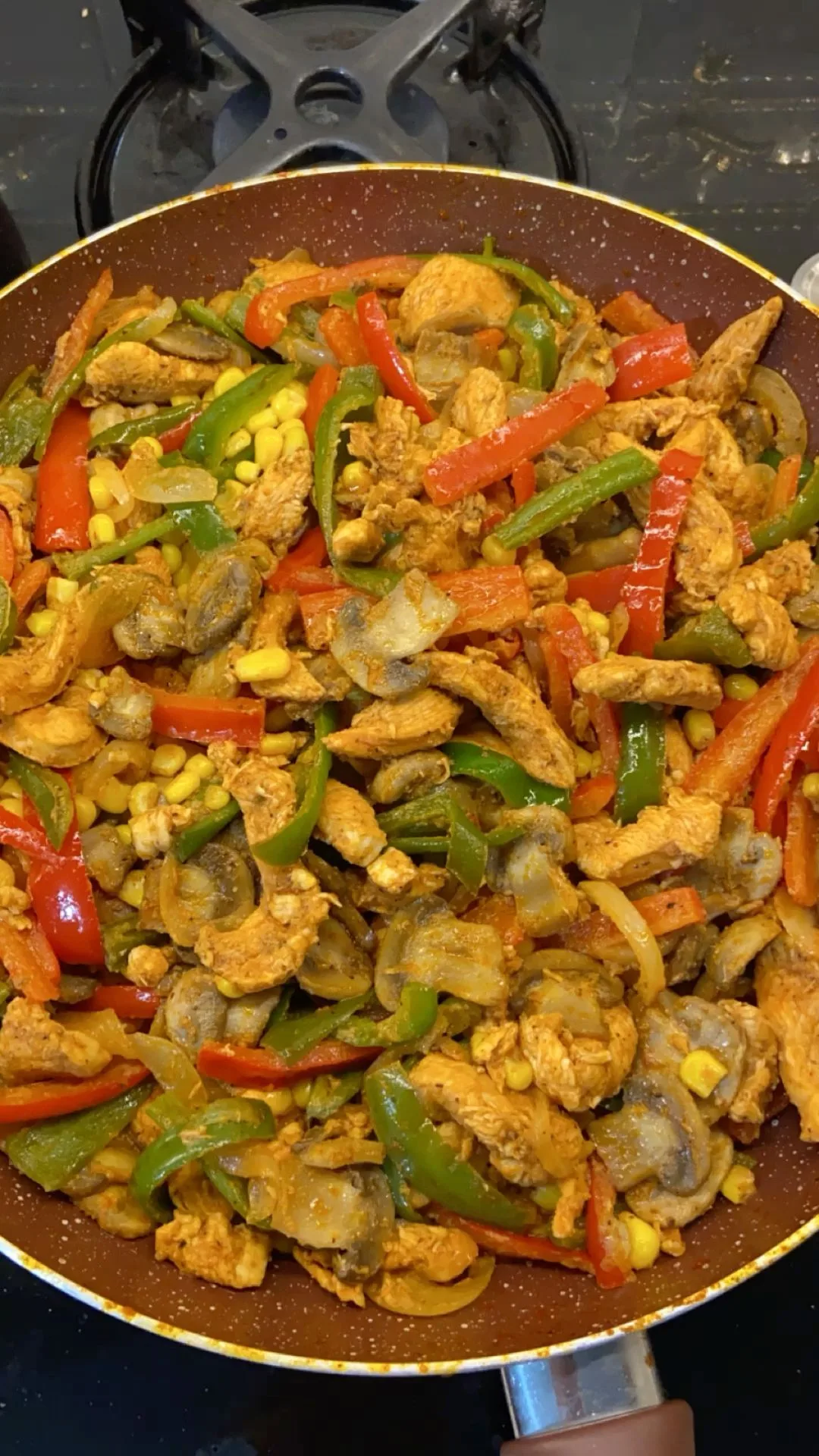 Une poêlée de poulet aux poivrons colorés, champignons et maïs dans une poêle antiadhésive.