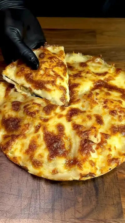 Une main gantée soulève une part de pizza ronde généreusement garnie de fromage fondu sur une planche en bois.