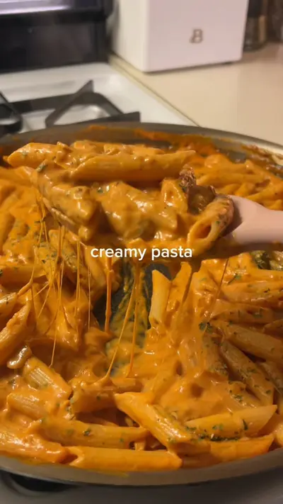 Une spatule soulève des penne enrobées d'une sauce tomate crémeuse orange avec des fils de fromage fondu.